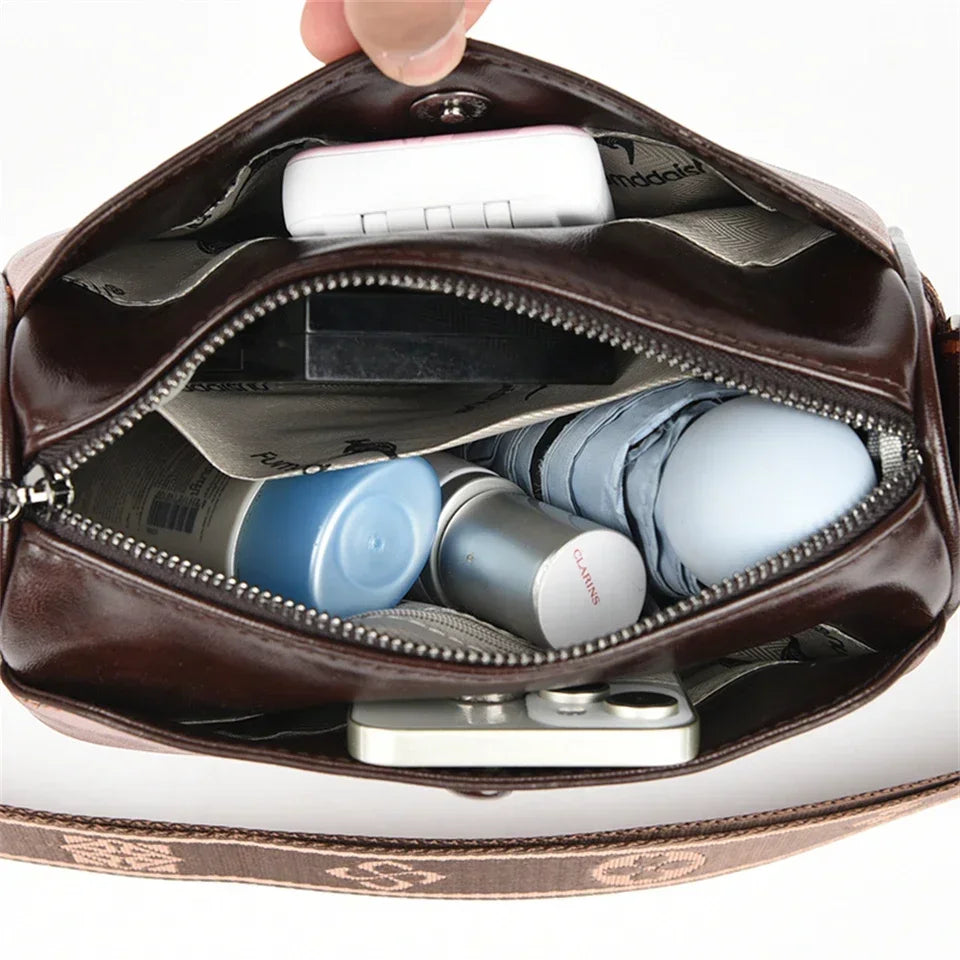 Sac bandouliere cuir femme élégant avec une poche zippée ouverte, montrant des produits de beauté à l'intérieur.