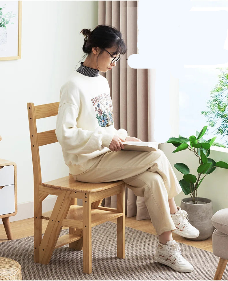 Femme assise sur une chaise pliante en bois, lisant un livre dans un intérieur lumineux et moderne.