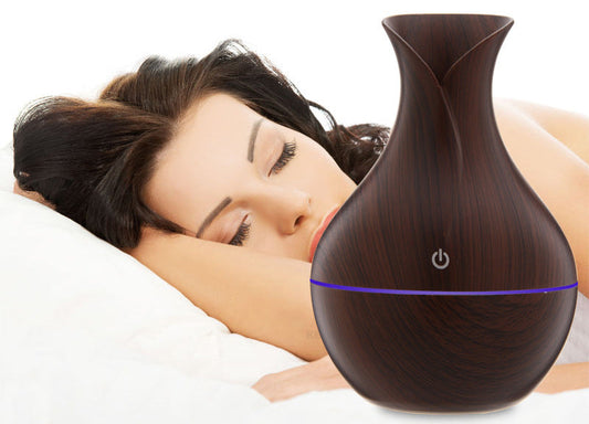 Diffuseur huiles essentielles design bois placé sur une table, créant une ambiance relaxante avec une personne se reposant à côté