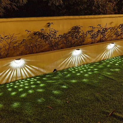 Applique murale solaire installée sur un mur avec des motifs lumineux sur la pelouse, créant une ambiance extérieure agréable