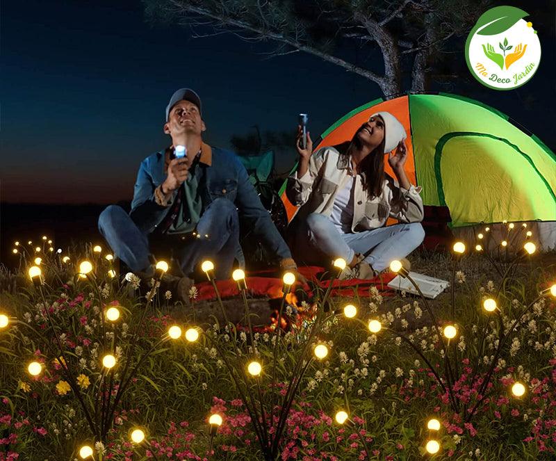 Lampe solaire décorative jardin illuminant une scène de camping élégante avec des couples assis entourés de fleurs et d'une tente colorée