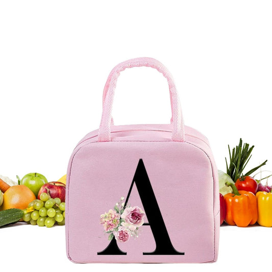 Sac isotherme rose avec motif floral et lettre A, idéal pour le transport des repas, en arrière-plan des fruits frais